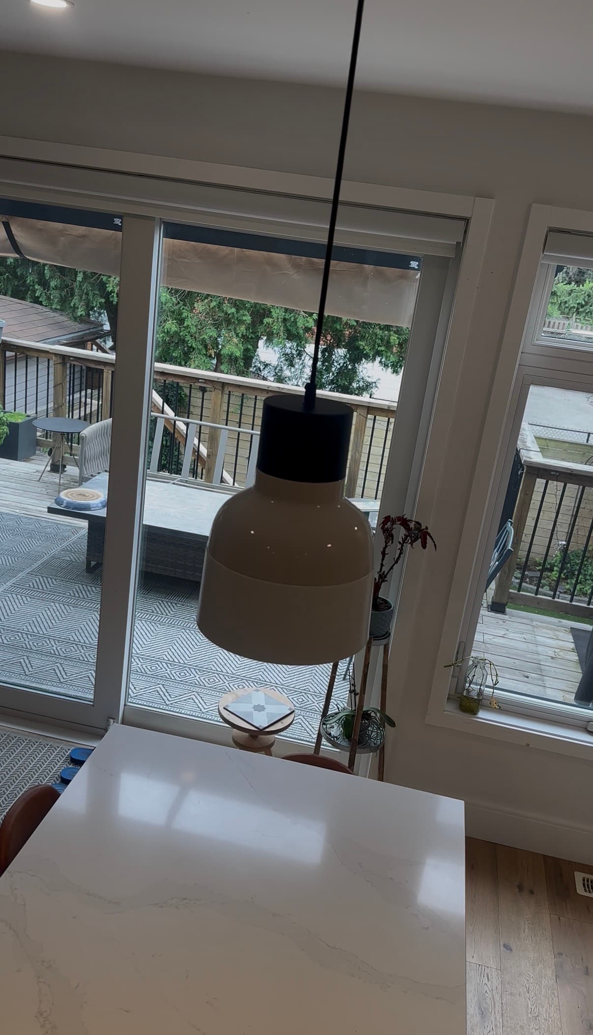 Modern white pendant light hanging over a marble island with a view of a wooden deck.