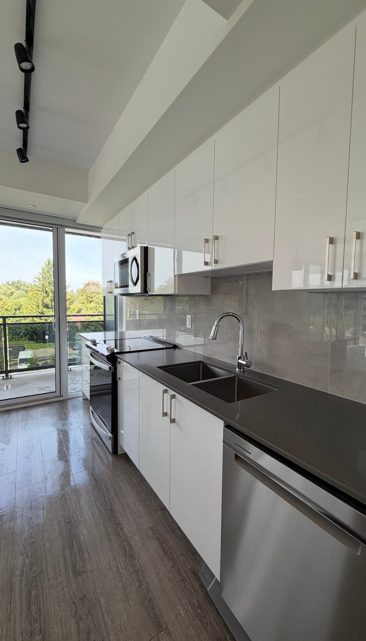 Modern kitchen featuring white cabinets, dark countertops, stainless steel appliances, and a balcony view.